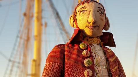 A handcrafted puppet of an 18th Century botanist with a boat in the background.